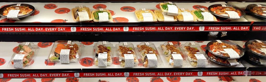 Sushi in plastic containers on display on grocery store shelves.