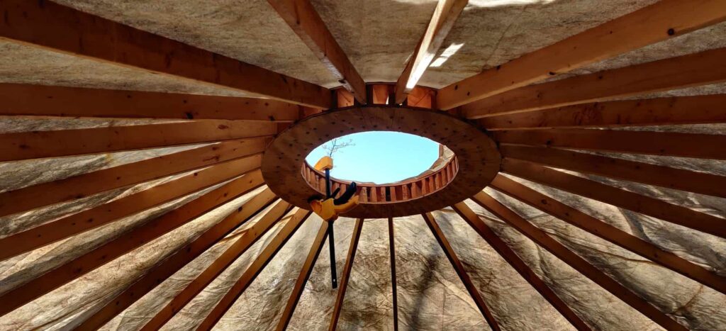 Interior of the roof of a yurt, with a clamp holding the covering to the yurt's roof ring. The sky is visible through the hold within the ring.