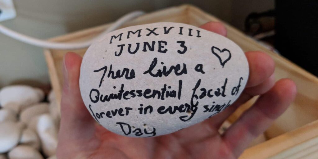 White, egg-shaped rock written with: MMXVIII June 3: There lives a quintessential facet of forever in every single day