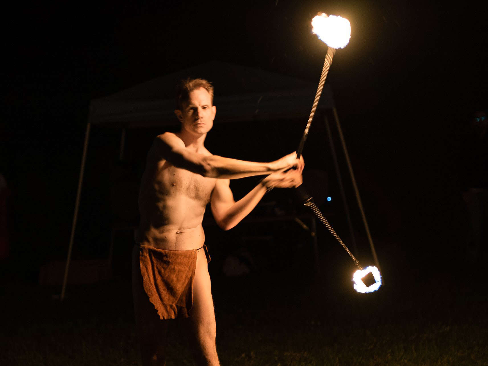 Mickey in a loincloth performing at night with fire poi.