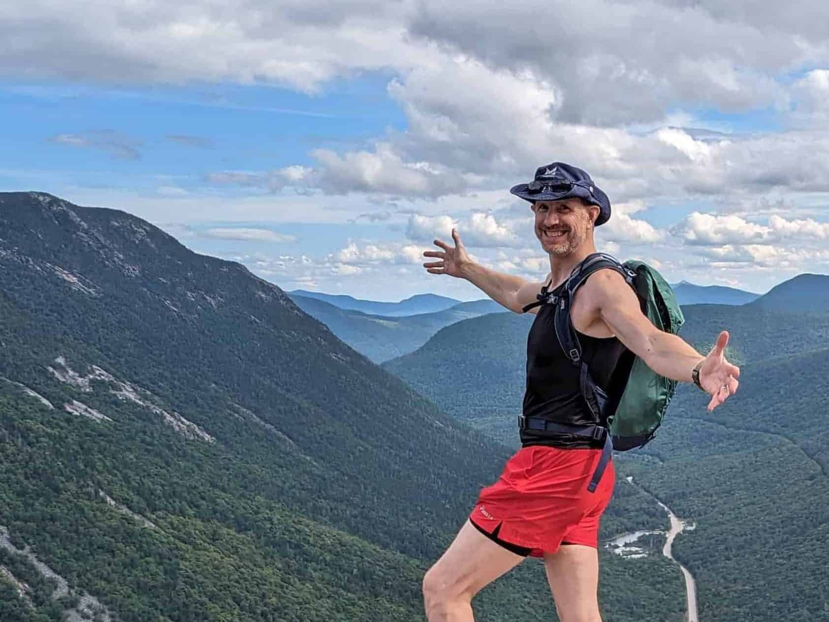 Mickey standing at the summit of Mount Willard in New Hampshire with a valley behind him.