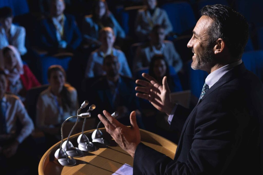 Side view of businessman standing and giving speech to live audience