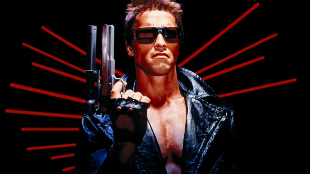 Arnold Schwarzenegger in a black jacket over a bare chest posing with a pistol for the movie, The Terminator.