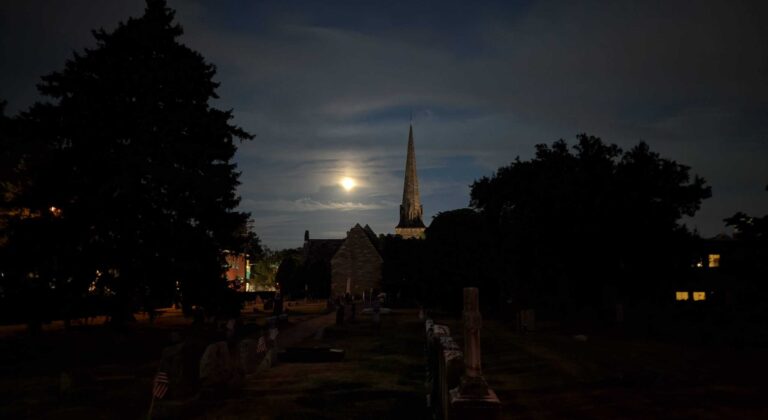 Moon over a church steeple with a cemetery in the foreground.