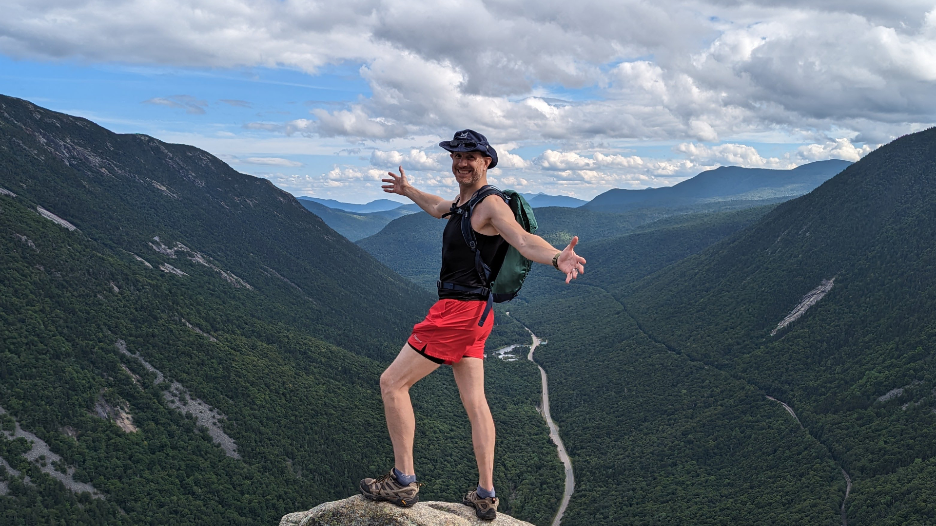 Mickey standing at the summit of Mount Willard in New Hampshire with a valley behind him